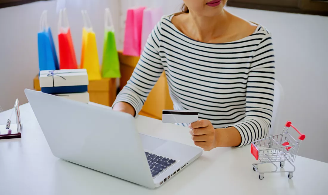 midsection-businesswoman-holding-credit-card-while-using-laptop-table