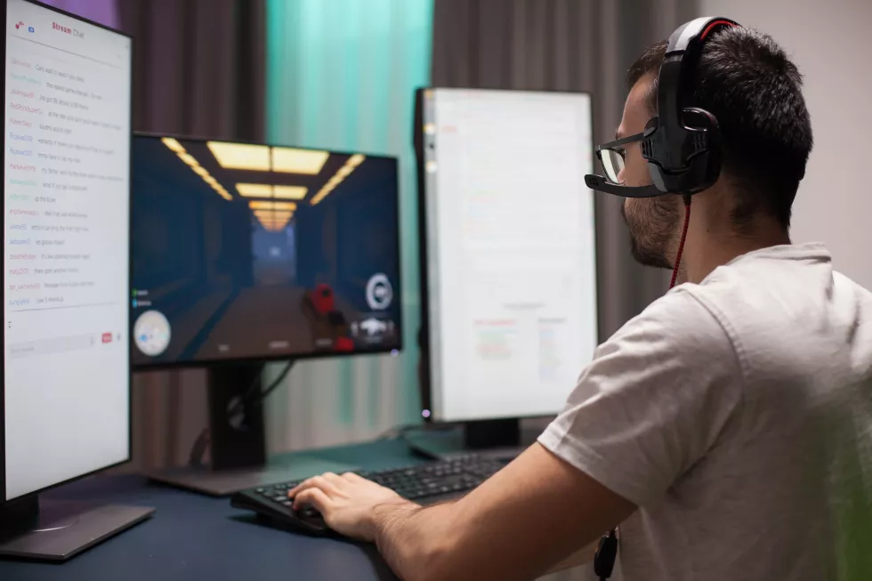 man-with-eyeglasses-wearing-headphones-while-playing-shooter-games-reading-streaming-chats-dual-screen-setup