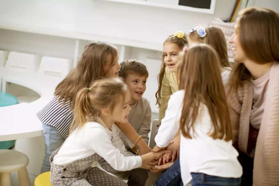 group-cute-preschool-kids-put-hands-together-with-their-nursery-teacher