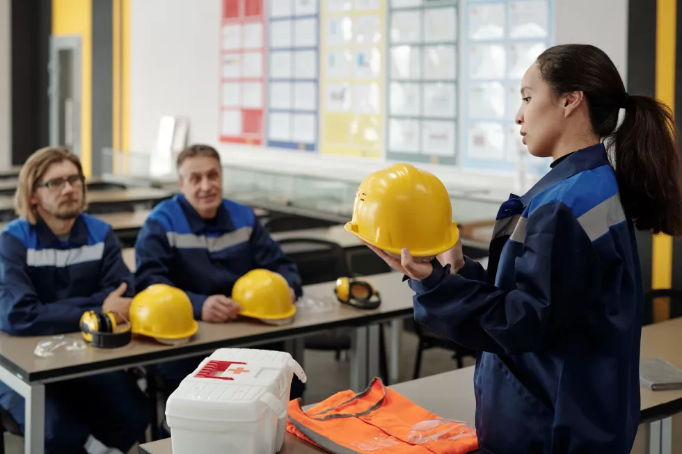 young-pretty-female-worker-uniform-standing-front-her-male-colleagues-while-describing-purpose-usage-protective-helmet