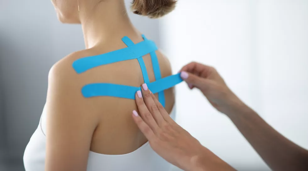 physiotherapist-doctors-hands-stick-blue-kinesio-tape-back-young-girl-patient-closeup