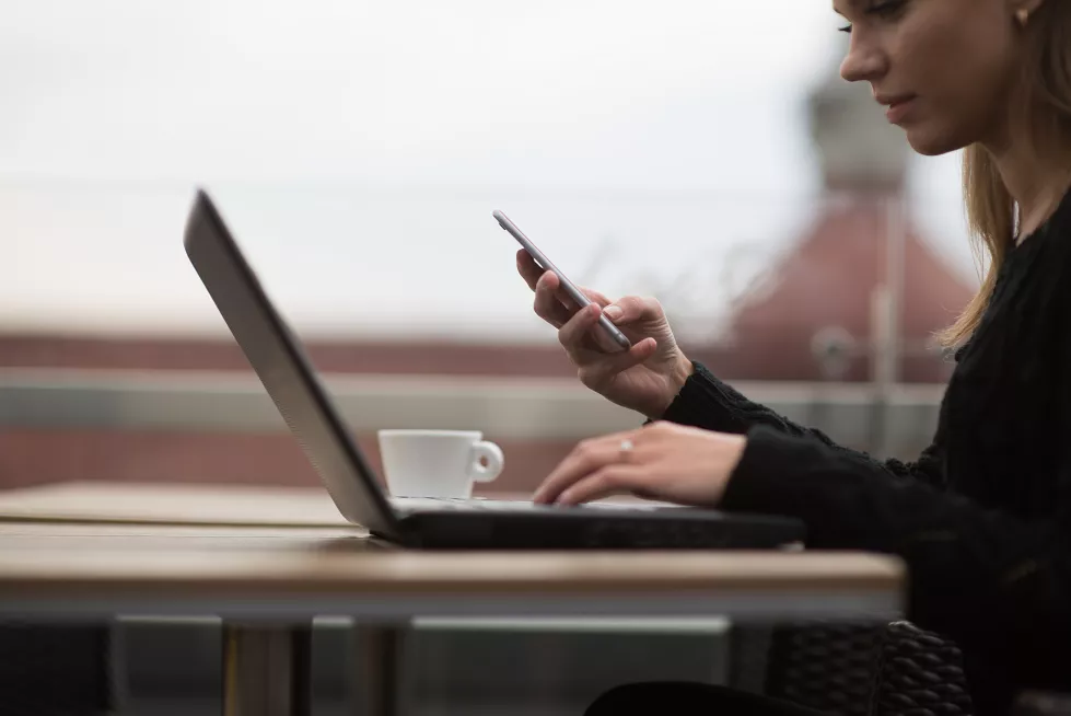 side-view-woman-using-mobile-phone-laptop-while-sitting-sidewalk-cafe