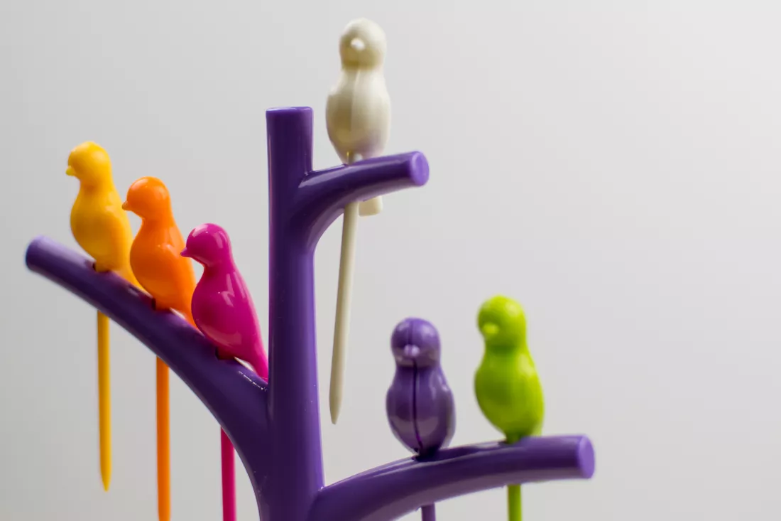 multicolored-plastic-bird-figures-sitting-tree-light-background