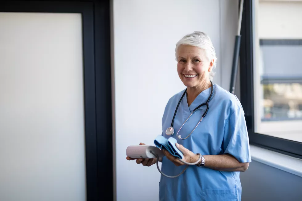 senior-female-nurse-holding-blood-pressure-monitor-cuff-clinic-window-copy-space