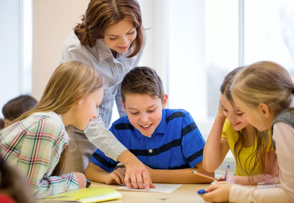 education-elementary-school-learning-people-concept-teacher-helping-school-kids-writing-test-classroom-2