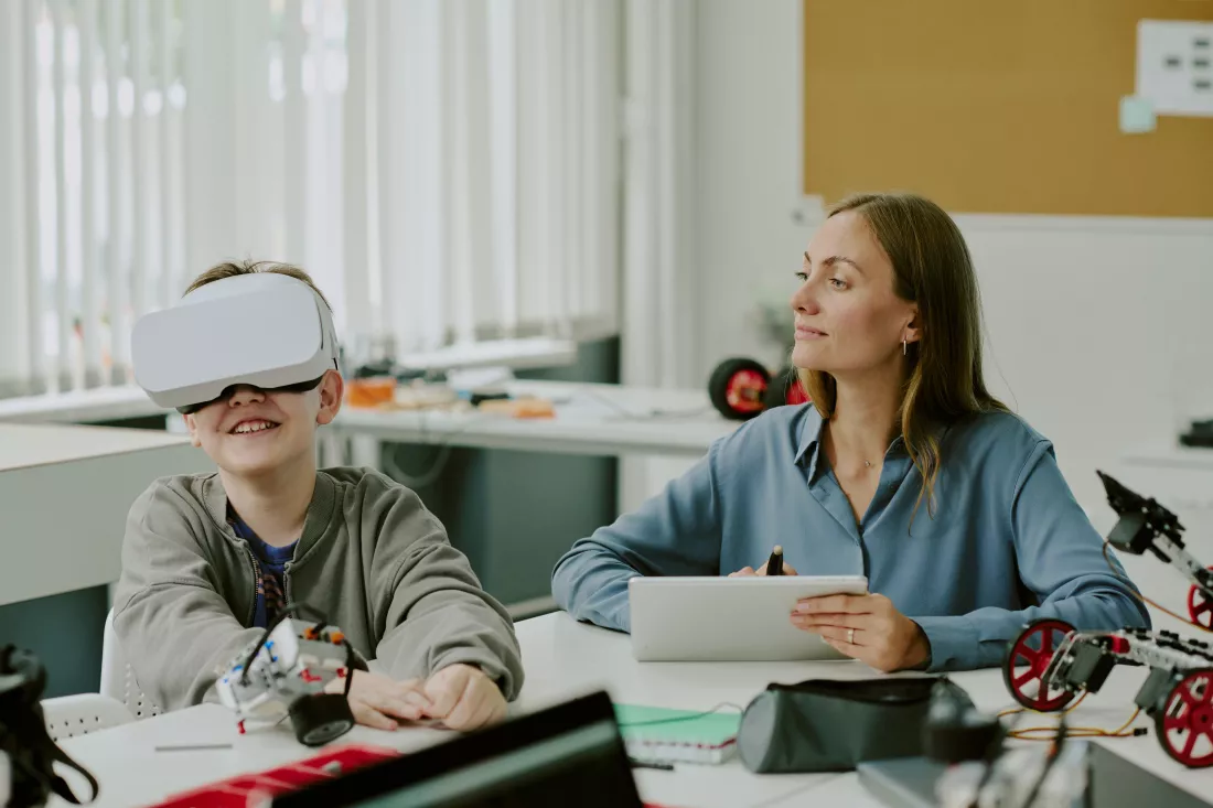 teacher-with-tablet-hands-looking-boy-playing-vr-game-smiling-widely