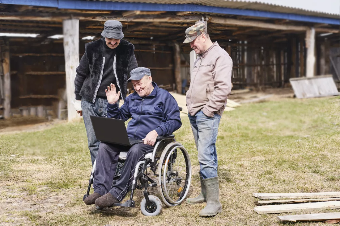 happy-senior-man-wheelchair-yard-looking-laptop-two-friends-are-standing-near