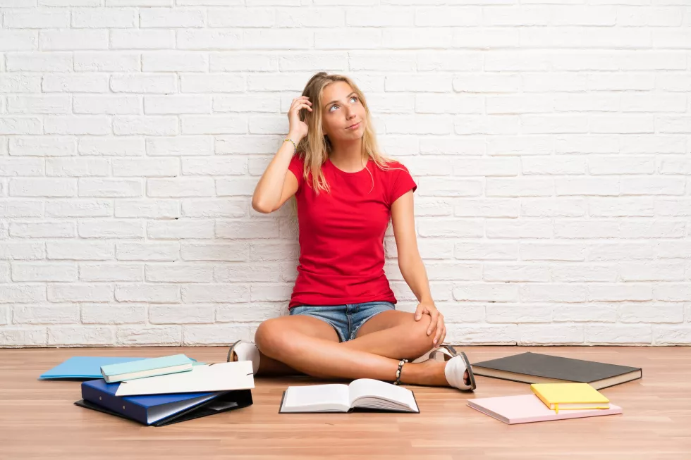 young-blonde-student-girl-with-many-books-floor-having-doubts-with-confuse-face-expression