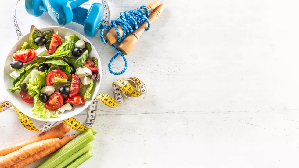 healthy-salad-with-tomatoes-surrounded-with-exercise-equipment-carrot-celery-measuring-tape