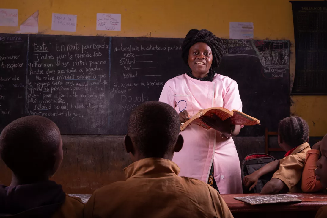 black-female-teacher-stands-front-explains-lesson-by-reading-from-book-from-desk