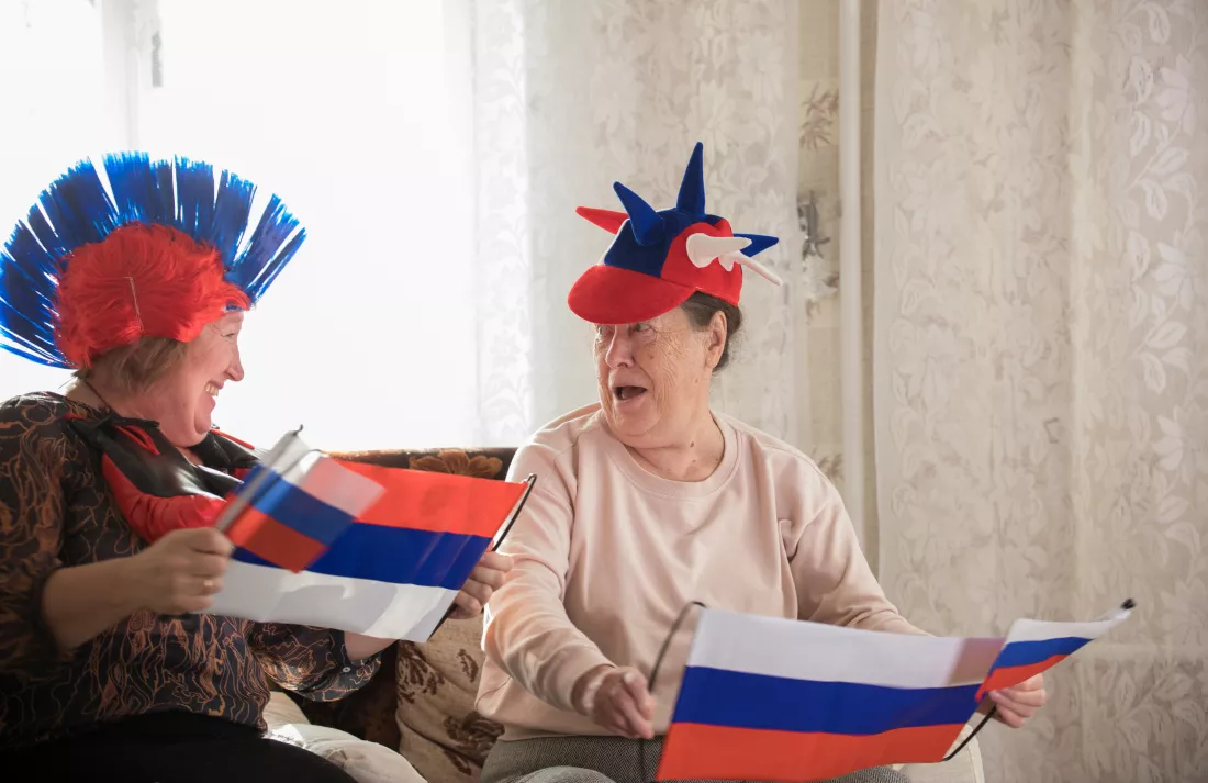 two-elderly-smiling-women-sitting-russian-accessories-holding-russian-flags