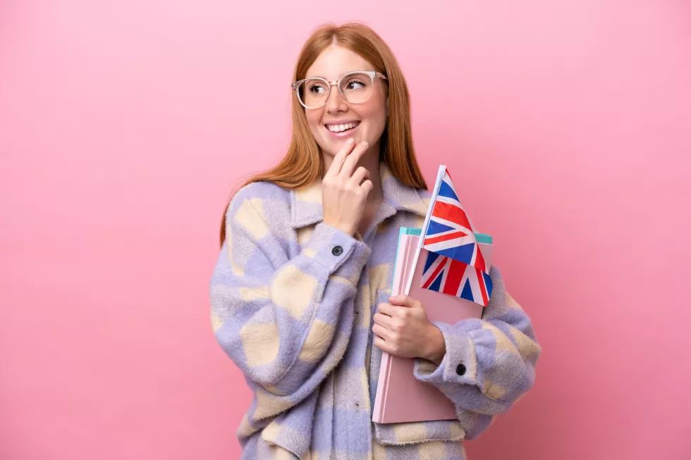 young-redhead-woman-holding-united-kingdom-flag-isolated-pink-background-looking-up-while-smiling